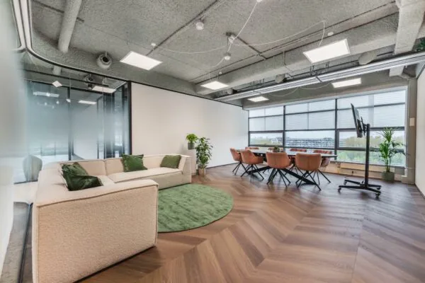 Moderne vergaderruimte aan de Joop Geesinkweg met een zithoek, grote ramen en een houten visgraatvloer.